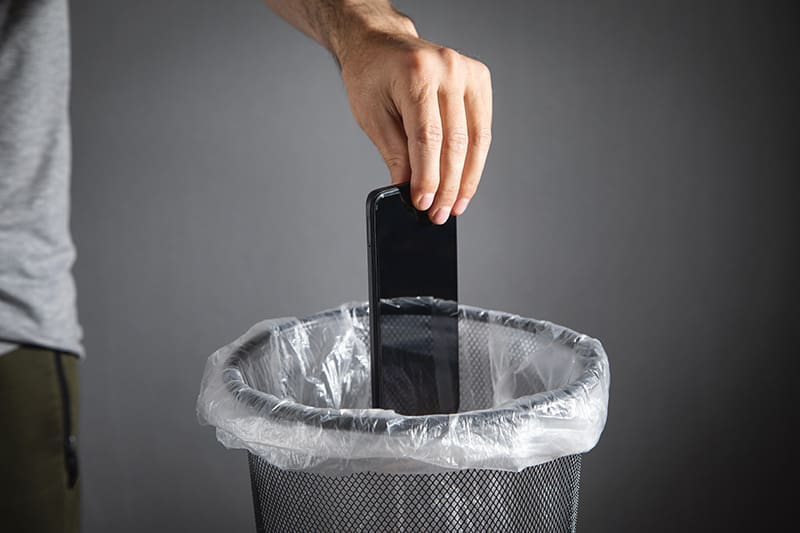 Main jetant un téléphone mobile dans une poubelle.